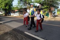 Foto/Dok: Petugas Polsek Manding, Aipda Moh. Karis, saat membantu menyeberangkan siswa SDN Manding Laok 1. @sumber_RADAR9.ID