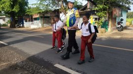 Foto/Dok: Petugas Polsek Manding, Aipda Moh. Karis, saat membantu menyeberangkan siswa SDN Manding Laok 1. @sumber_RADAR9.ID