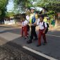 Foto/Dok: Petugas Polsek Manding, Aipda Moh. Karis, saat membantu menyeberangkan siswa SDN Manding Laok 1. @sumber_RADAR9.ID
