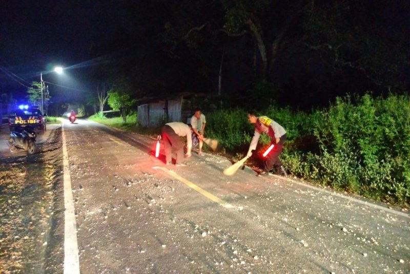 Foto: Dua anggota Polsek Manding bersama warga sigap membersihkan tumpahan batu cor yang berserakan di Jalan Raya Desa Jabaan, guna mencegah risiko kecelakaan. Dokumentasi RADAR9.ID/Redaksi.